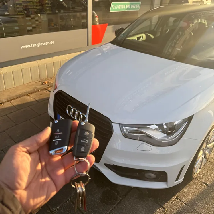 Audi Ersatzschlüssel angefertigt, in der Hand haltend und Auto im Hintergrund - Kundenauftrag