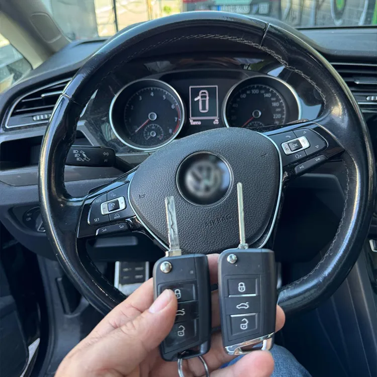 Nachgemachter VW Autoschlüssel in der Hand, Lenkrad im Hintergrund